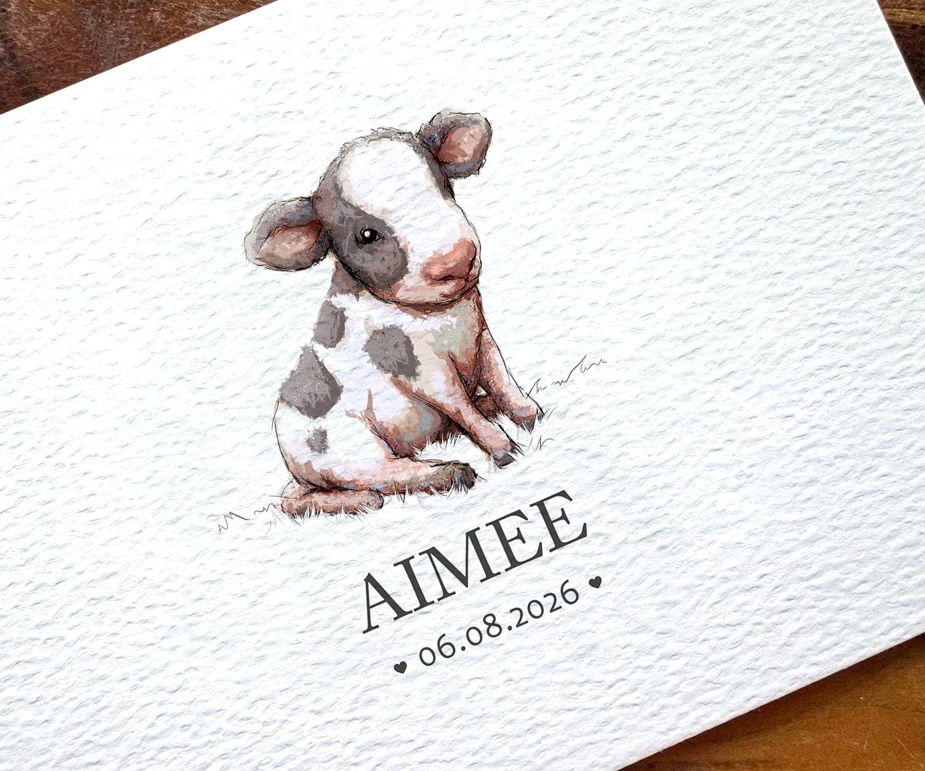 A close-up of a personalized baby shower card featuring a watercolor illustration of a black and white calf. The card is printed with the name 'AIMEE' and the date '06.