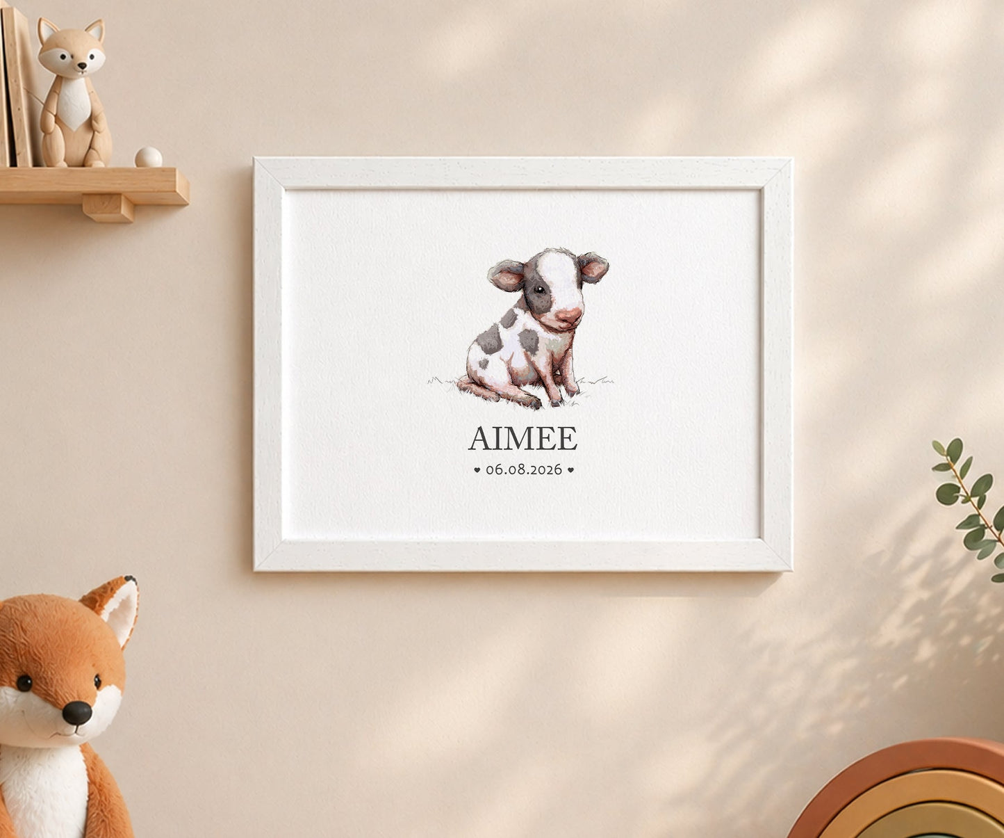 A framed personalized art print featuring a watercolor illustration of a baby cow with the name 'AIMEE' and the date '06.08.