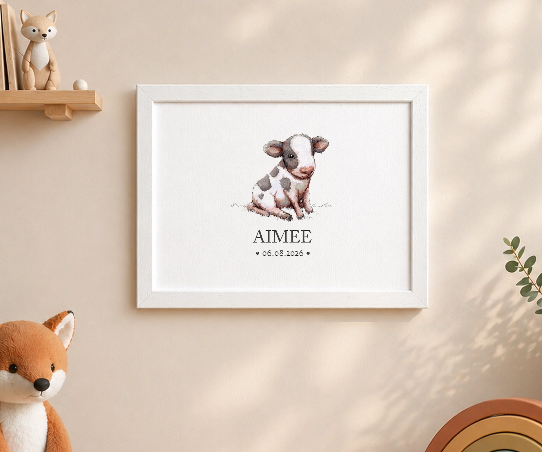 A framed personalized art print featuring a watercolor illustration of a baby cow with the name 'AIMEE' and the date '06.08.