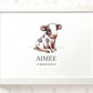 A framed personalized watercolor print featuring a cute black-and-white calf illustration with the name 'AIMEE' and the date '06.08.