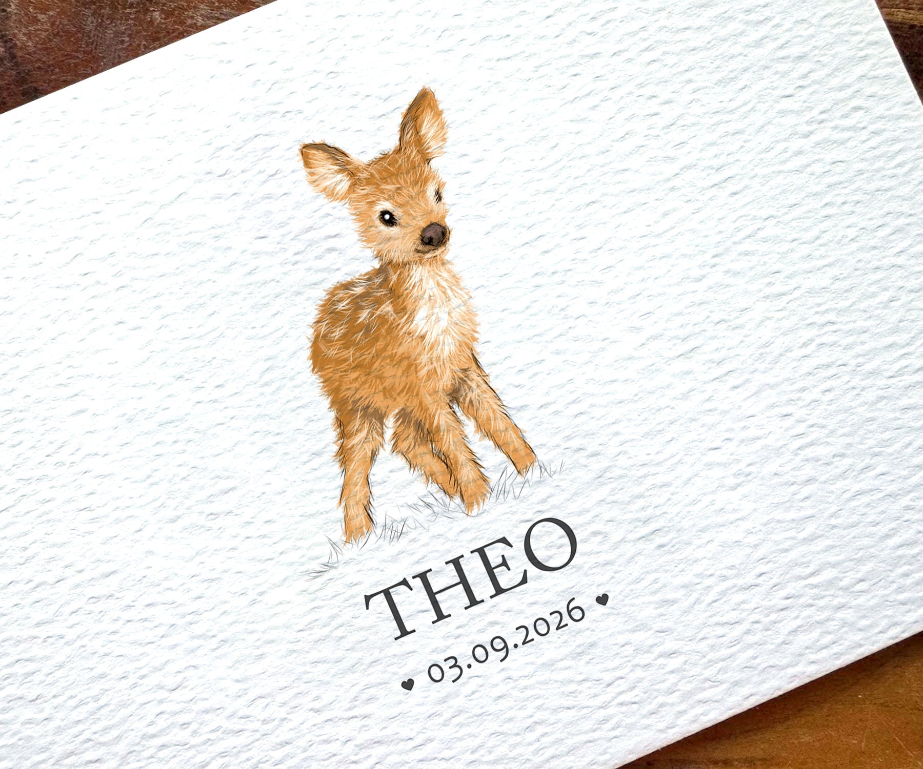 A close-up of a personalized white textured card featuring a watercolor illustration of a young brown deer and the printed name 'THEO' with the date '03.09.