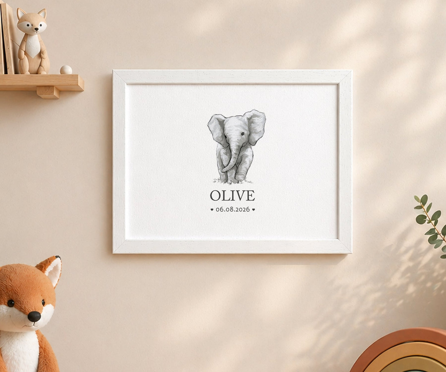 A framed personalized elephant art print hanging on a beige wall, featuring a gray watercolour-style elephant illustration with the name 'OLIVE' and the date '06.08.