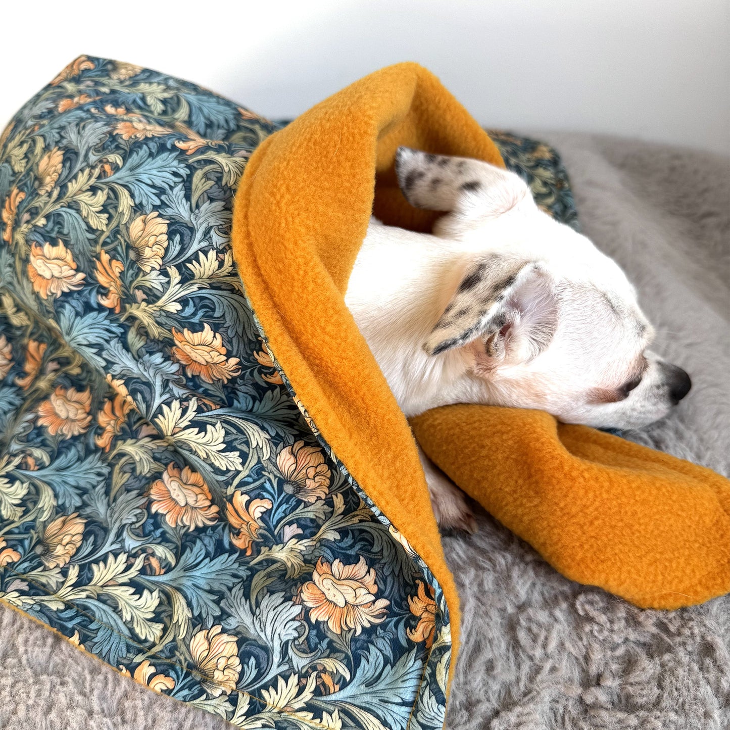 Dog wrapped in handmade dog blanket with patterned cotton top and ochre fleece lining