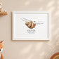 A framed personalized art print featuring a watercolor sloth hanging from a branch with the name 'OLIVIA' and the date '06.05.